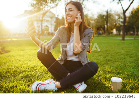 The girl holds the phone and coffee in hand. Sunset. Summertime. 102239645