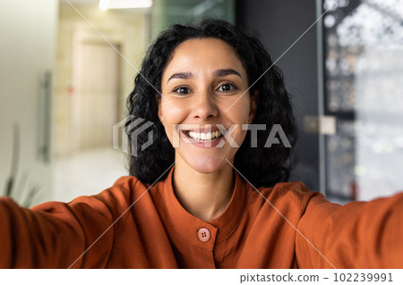 Business woman in the office talking on a video call, using application on smartphone for online remote communication, looking at the camera and smiling, a Latin American inside . Business woman in the office talking on a video call, using application on smartphone for online remote communication, looking at the camera and smiling, a Latin American inside . 102239991