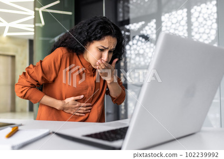 Sick business woman working at work, having severe nausea and abdominal pain, latin american working inside office building using laptop Sick business woman working at work, having severe nausea and abdominal pain, latin american working inside office building using laptop 102239992