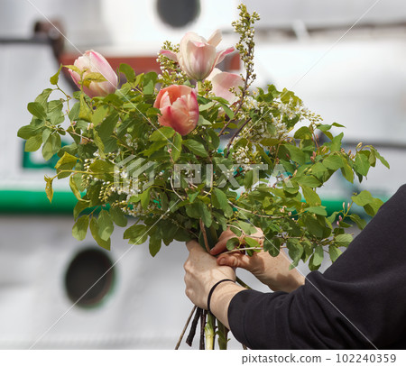 A florist ties a bouquet at a farmers market, a womans hands holding a large tied bouquet. A florist ties a bouquet at a farmers market, a womans hands holding a large tied bouquet. 102240359