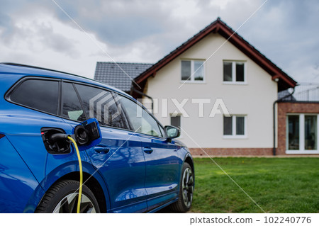 Close-up of electric car charging near family house. Close-up of electric car charging near family house. 102240776