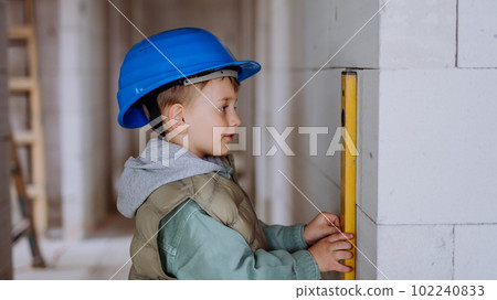 Little boy in unfinished house measuring wall in unfinished house with spirit level. Little boy in unfinished house measuring wall in unfinished house with spirit level. 102240833