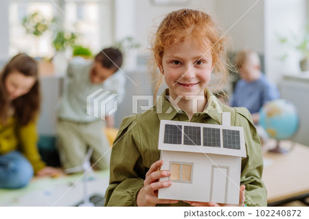 Little girl posing with model of house with solar system during a school lesson. 102240872