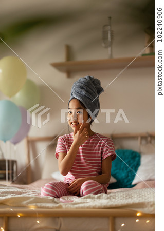 Little girl sitting on her bed and appling beauty mask on her face. 102240906