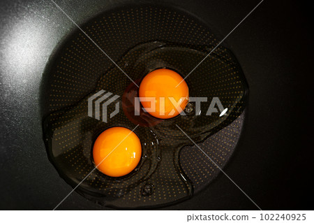 Two raw eggs with yellow yolks on the black frying pan ready to cook. Delicious healthy simple breakfast meal. Traditional homemade quick breakfast. International cuisine food. Top view. Two raw eggs with yellow yolks on the black frying pan ready to cook. Delicious healthy simple breakfast meal. Traditional homemade quick breakfast. International cuisine food. Top view. 102240925