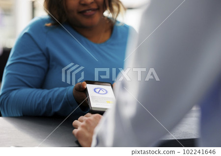 African american woman using phone nfc to pay for stylish items on pos terminal, buying fashionable clothes and accessories in modern boutique. Shopper standing at retail store counter desk. Close up African american woman using phone nfc to pay for stylish items on pos terminal, buying fashionable clothes and accessories in modern boutique. Shopper standing at retail store counter desk. Close up 102241646