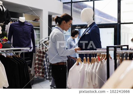 Asian worker looking at hangers with casual wear, arranging fashionable clothes before store opening. Employee wearing formal shirt, working with trendy merchandise in modern boutique. Fashion concept 102241666