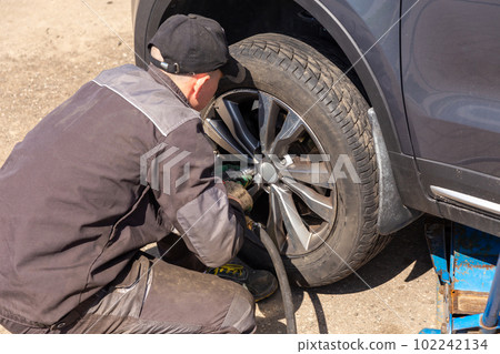 Mechanician changing car wheel in auto repair shop. 102242134