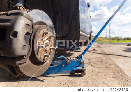 Car on tire mounting with removed wheel on pneumatic jack, seasonal tire change, car service concept. Car on tire mounting with removed wheel on pneumatic jack, seasonal tire change, car service concept. 102242138