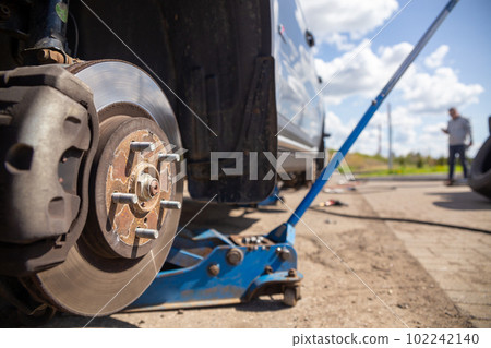 Car on tire mounting with removed wheel on pneumatic jack, seasonal tire change, car service concept. Car on tire mounting with removed wheel on pneumatic jack, seasonal tire change, car service concept. 102242140