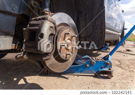 Car on tire mounting with removed wheel on pneumatic jack, seasonal tire change, car service concept. 102242141