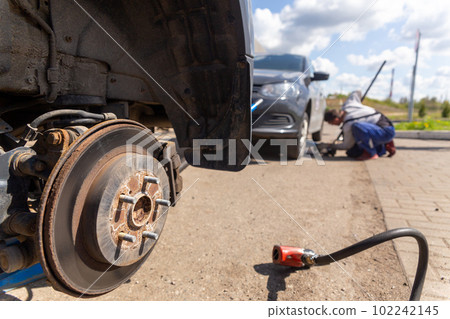 Car on tire mounting with removed wheel on pneumatic jack, seasonal tire change, car service concept. 102242145
