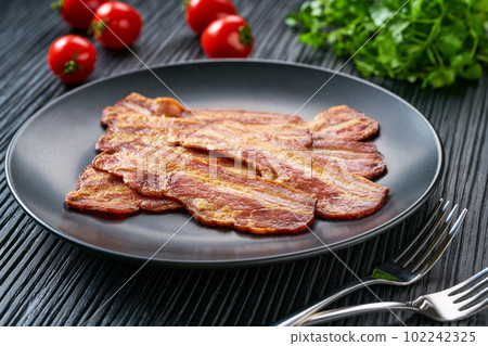plate with fried bacon and bbq sauce on a black table.  Plate with fried bacon on black  kitchen table. 102242325