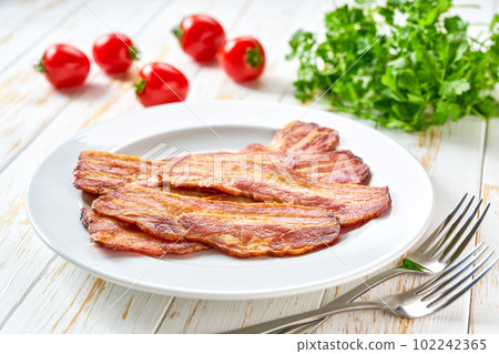 fried bacon strips with bbq sauce in a dish on a white table. fried bacon strips with bbq sauce in a dish on a white table. 102242365