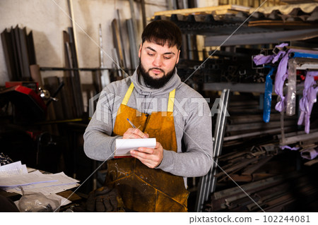 Craftsman of metalworking shop writing in notebook 102244081