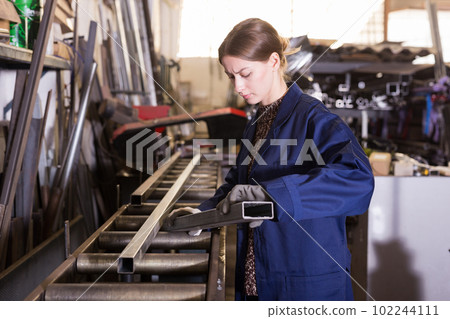 Female worker cuts metal profile pipe on a band saw Female worker cuts metal profile pipe on a band saw 102244111