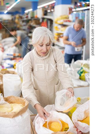 Old woman purchaser buying crushed corn in big supermarket 102244273