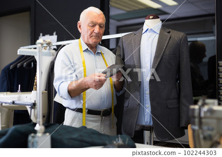 Experienced tailor threading jacket before starting work in workshop 102244303