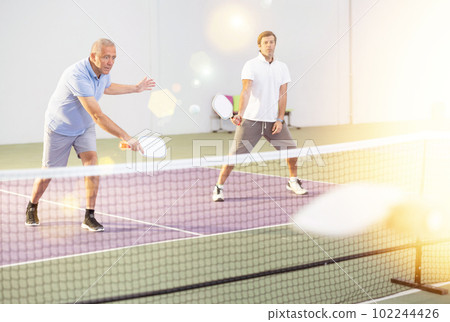 Aged man playing doubles pickleball match with male partner Aged man playing doubles pickleball match with male partner 102244426