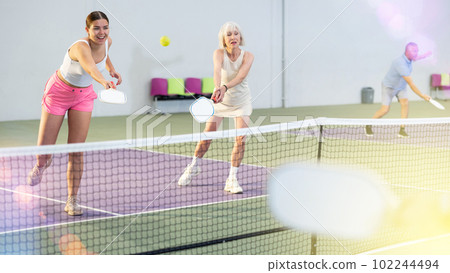 Girl playing doubles pickleball in team with older woman indoors 102244494