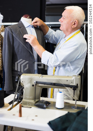 Experienced tailor tries on a new jacket on a mannequin in sewing atelier 102244534