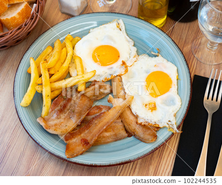 Close up of grilled bacon with fried potato and egg served on blue plate 102244535