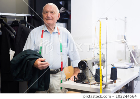 Portrait of an accomplished elderly tailor at his workplace in sewing workshop 102244564