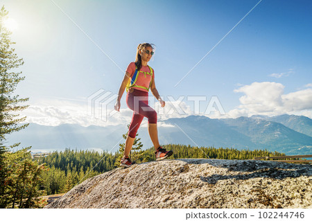 Hiking people. Woman hiker on mountain hike trail enjoying view wearing backpack and hiking clothing in beautiful blue sky nature landscape. Squamish hike, British Columbia, Canada. Hiking people. Woman hiker on mountain hike trail enjoying view wearing backpack and hiking clothing in beautiful blue sky nature landscape. Squamish hike, British Columbia, Canada. 102244746