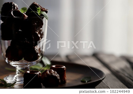 Mini canelés and mint leaves spilling from a stemware glass Mini canelés and mint leaves spilling from a stemware glass 102244949