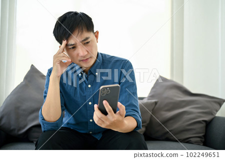 Stressed and thoughtful Asian man looking at his smartphone. bad news, no internet connection Stressed and thoughtful Asian man looking at his smartphone. bad news, no internet connection 102249651