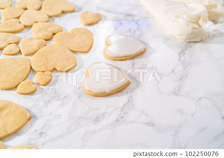 Decorating heart-shaped sugar cookies with pink and white royal icing for Valentine's Day. Decorating heart-shaped sugar cookies with pink and white royal icing for Valentine's Day. 102250076