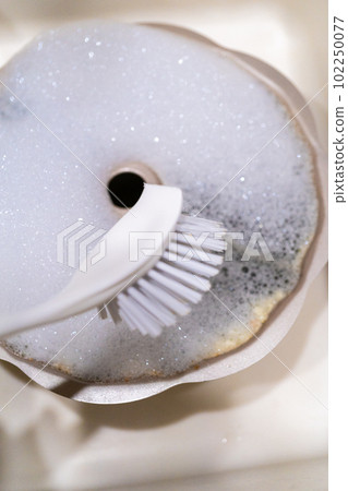 Scrubbing dirty aluminum bundt cake pan with kitchen scrub brush in a kitchen sink. Scrubbing dirty aluminum bundt cake pan with kitchen scrub brush in a kitchen sink. 102250077