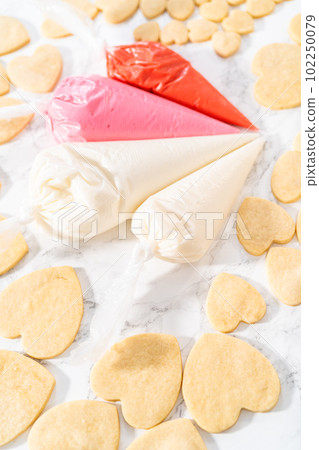 Decorating heart-shaped sugar cookies with pink and white royal icing for Valentine's Day. Decorating heart-shaped sugar cookies with pink and white royal icing for Valentine's Day. 102250079