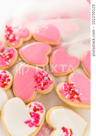Storing heart-shaped sugar cookies with pink and white royal icing in a large plastic container. Storing heart-shaped sugar cookies with pink and white royal icing in a large plastic container. 102250128