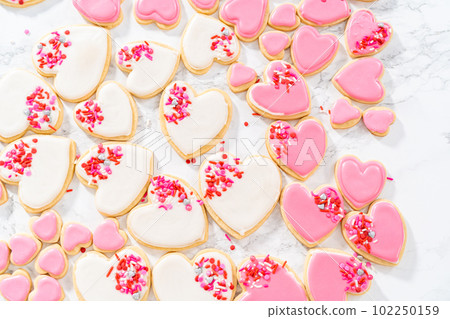 Decorating heart-shaped sugar cookies with pink and white royal icing for Valentine's Day. Decorating heart-shaped sugar cookies with pink and white royal icing for Valentine's Day. 102250159