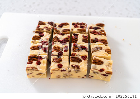 Cutting white chocolate cranberry pecan fudge into small pieces on a white cutting board. Cutting white chocolate cranberry pecan fudge into small pieces on a white cutting board. 102250181
