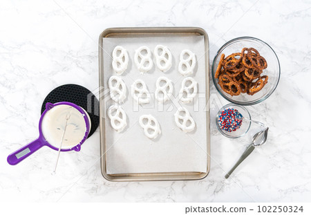 Flat lay. Dipping pretzels twists into melted chocolate to make red, white, and blue chocolate-covered pretzel twists. Flat lay. Dipping pretzels twists into melted chocolate to make red, white, and blue chocolate-covered pretzel twists. 102250324