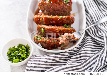 Slicing classic meatloaf with a sweet glaze on a white serving plate 102250430