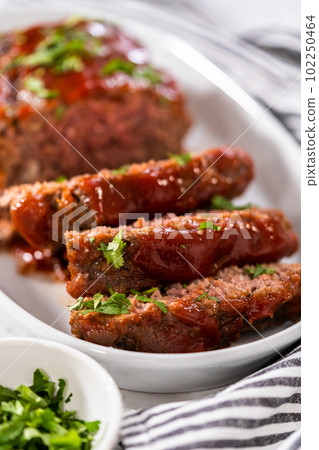 Slicing classic meatloaf with a sweet glaze on a white serving plate 102250464