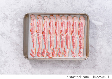 Flat lay. Uncooked bacon strips on a baking sheet with white parchment paper. Flat lay. Uncooked bacon strips on a baking sheet with white parchment paper. 102250601