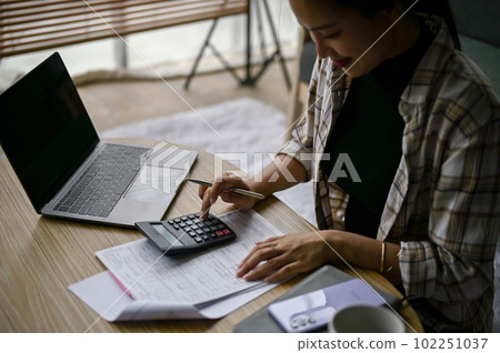 A woman calculating taxes and expenses in a living room. 102251037