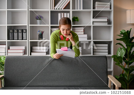 Focused Asian businesswoman leaning on a sofa in her office, reading documents 102251088