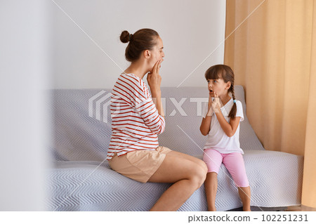 Indoor shot of female speech therapist working with little girl, training pronunciation of sounds and articulation, people wearing casual style clothing, sitting on sofa near window. Indoor shot of female speech therapist working with little girl, training pronunciation of sounds and articulation, people wearing casual style clothing, sitting on sofa near window. 102251231