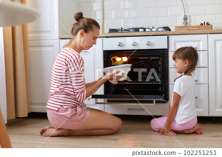 Indoor shot of woman and female child wearing casual clothing sitting on floor and smelling spoiled dessert, expressing negative emotions, cooking at home together. Indoor shot of woman and female child wearing casual clothing sitting on floor and smelling spoiled dessert, expressing negative emotions, cooking at home together. 102251251