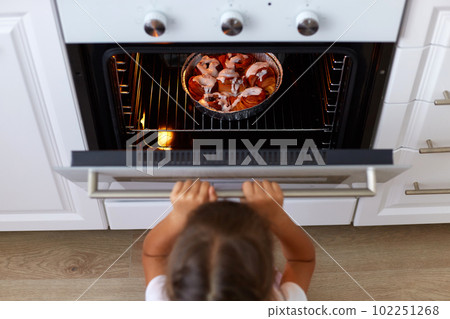 Top view of girl child opening oven looking at tasty croissant or other baking n the oven, cooking process on kitchen, small dark haired female kid wants delicious sweets. Top view of girl child opening oven looking at tasty croissant or other baking n the oven, cooking process on kitchen, small dark haired female kid wants delicious sweets. 102251268