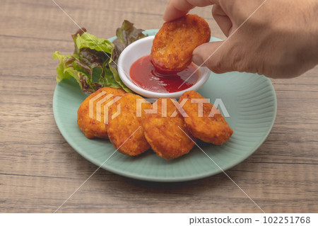 Chicken nuggets and ketchup are served on a blue plate Holding a nugget and dipping it in ketchup Chicken nuggets and ketchup are served on a blue plate Holding a nugget and dipping it in ketchup 102251768
