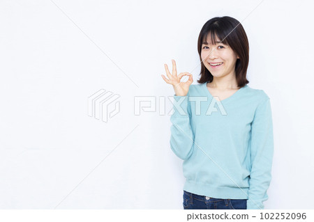 A woman in her thirties doing an OK sign in front of a white background 102252096