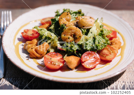 Warm salad with shrimps and salmon, sauce and parmesan on top. Healthy food outdoor 102252405