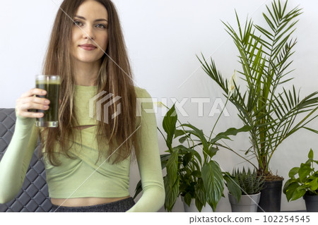A beautiful young woman is holding a glass of green juice or smoothie for weight loss. 102254545