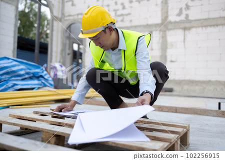 Young Asian engineer in engineering uniform and helmet at construction site working on architecture design blueprint. 30s professional foreman working on structure building at workplace 102256915